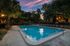 Evening view of a tranquil swimming pool surrounded by lush trees and comfortable loungers.