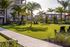 Lush green garden with palm trees, cozy seating, and a modern apartment complex in the background.