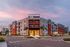 Modern apartment complex at sunset with palm trees and ample parking.