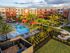 Beautiful apartment complex with landscaped gardens and large pool area, surrounded by palm trees.
