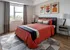 Stylish bedroom with vibrant orange bedding, modern artwork, and natural light from a large window.