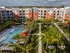 Overview of modern apartment complex with pool, lush gardens, and palm trees.