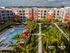 Aerial view of a modern apartment complex with a large swimming pool, lush gardens, and sleek architecture.