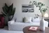 Chic living room with a cozy white sofa, stylish pillows, vibrant green plants, and a contemporary table lamp creating a serene ambiance.