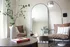 Modern apartment corner with elegant seating, an arched mirror, and stylish decor including a sleek floor lamp and a vase with green branches on a wooden table.