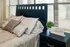 Cozy bedroom with elegant bedding, stylish dark wood headboard, and decorative accents, well-lit with natural sunlight.