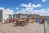 Vibrant rooftop terrace with stylish wooden seating and breathtaking cityscape views under a clear blue sky.