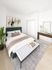 Elegant bedroom with a plush green bed, cozy white bench, modern artwork, and stylish decor. Bright and inviting space perfect for relaxation.