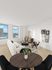 Bright and airy living space with modern decor, featuring large windows with city views, a cozy white sofa, stylish dining area, and elegant wooden furnishings.