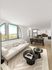 Bright and modern living area with large arched windows, stylish sofa, chic black coffee tables, and an open-concept kitchen featuring elegant cabinetry and dining space.
