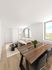 Bright, modern living and dining area with stylish wooden table, elegant gray chairs, cozy sofa, and large windows letting in natural light.