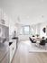 Modern apartment kitchen featuring sleek white cabinetry, stainless steel appliances, and a sunlit dining area with city views.