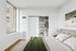 Bright and cozy bedroom with sleek built-in closet and modern art on the wall, offering a serene urban view.