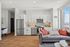 Chic open-plan kitchen and living area with modern white cabinetry, sleek stainless steel appliances, and a cozy sofa adorned with vibrant cushions, offering stunning city views through large windows.