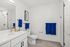 Sleek modern bathroom with elegant white cabinetry and vibrant blue towels, featuring a spacious mirror and chic shower area.