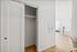 Bright and modern apartment interior showcasing a sleek closet, elegant wooden flooring, and a glimpse into a cozy living area with stylish seating.