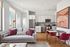 Bright and modern open-plan living space featuring elegant white cabinetry, stainless steel appliances, a cozy gray sofa with vibrant pillows, and stylish dining setup in a chic city apartment.