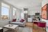 Bright modern apartment living room with large windows, chic gray sofa adorned with colorful cushions, and elegant kitchen with stainless steel appliances and stylish cabinetry.