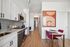 Sleek modern kitchen with white cabinets, stainless steel appliances, and stylish backsplash, adjacent to a cozy dining area with vibrant pink chairs.