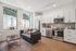 Chic urban apartment kitchen featuring sleek stainless steel appliances, modern cabinetry, and bright windows overlooking architectural details, complemented by a cozy sitting area with a stylish sofa and contemporary decor.