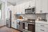 Modern kitchen with sleek stainless steel appliances, elegant white cabinetry, and stylish gray tile backsplash.
