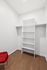 Modern walk-in closet with sleek white shelving and a stylish red chair on elegant wooden flooring.