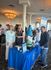 Vibrant networking event with smiling attendees and a whimsical gnome statue at a blue-branded display table.