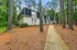 Charming townhouse nestled in serene wooded surroundings, with a welcoming pathway leading to the entrance.