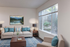 Bright and inviting lounge with chic modern furniture, vibrant blue accents, and scenic wall art, perfect for relaxation. Expansive window views of lush outdoor greenery enhance the serene ambiance.
