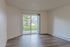 Bright living space with sleek hardwood floors and a large window showcasing lush green views.