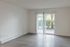 Bright apartment space with sleek wooden flooring and large sliding glass doors opening to lush greenery.