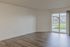 Bright and spacious living room with elegant wood flooring and large sliding glass doors leading to a green outdoor view.