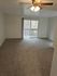 Spacious apartment room with plush carpeting, ceiling fan, and natural light streaming through sliding glass doors.