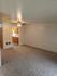 Spacious living room with plush carpet and ceiling fan, leading to a bright kitchen with wooden cabinets.