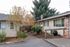 Charming suburban apartment exterior featuring a well-maintained brick and siding facade, framed by lush greenery and colorful autumn foliage.