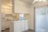 Bright and cozy kitchen with modern white cabinets, featuring a full-sized fridge and elegant marble countertops, connected to a sunlit dining area with vertical blinds.