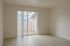 Bright, airy room with sleek wooden flooring and a large glass sliding door opening to a cozy private balcony.