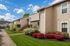 Charming apartment complex with lush green lawns, vibrant flower beds, and well-maintained exteriors against a bright blue sky.