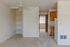 Bright apartment with cozy carpeted floors, built-in storage shelves, and modern ceiling fan, leading to an inviting, well-lit bedroom and functional kitchen area.