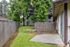 Charming garden space with lush trees and a chain-link fence, leading to a cozy apartment building with sliding glass doors.