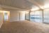Bright, spacious living room featuring plush carpet, large windows with vertical blinds, and elegant white walls.