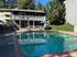 Inviting apartment pool area with sun loungers, umbrella, and lush greenery, perfect for relaxing under the sun.