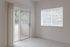 Bright, airy room with plush carpeting and large windows opening to a charming balcony with lush greenery view.