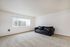 Bright and spacious living room featuring a sleek black leather sofa and large window with vertical blinds, perfect for letting in natural light.