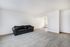 Spacious living room with plush carpeting, featuring a sleek black leather sofa and abundant natural light.