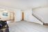 Bright and inviting living room with plush carpeting, leading to a modern staircase and an open area with natural light filtering through large windows.