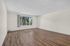 Spacious living room with elegant wood flooring and large window offering a serene garden view.