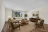 Bright and inviting living room with modern furniture, soft neutral tones, and a large window showcasing lush greenery.