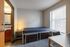 Cozy and modern bedroom with a minimalist design, featuring a sleek bed, ambient lighting, large window with blinds, and a peek into a stylish bathroom.