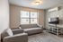 Modern apartment living room featuring sleek gray sofas, a mounted flat-screen TV, and large windows for natural light.